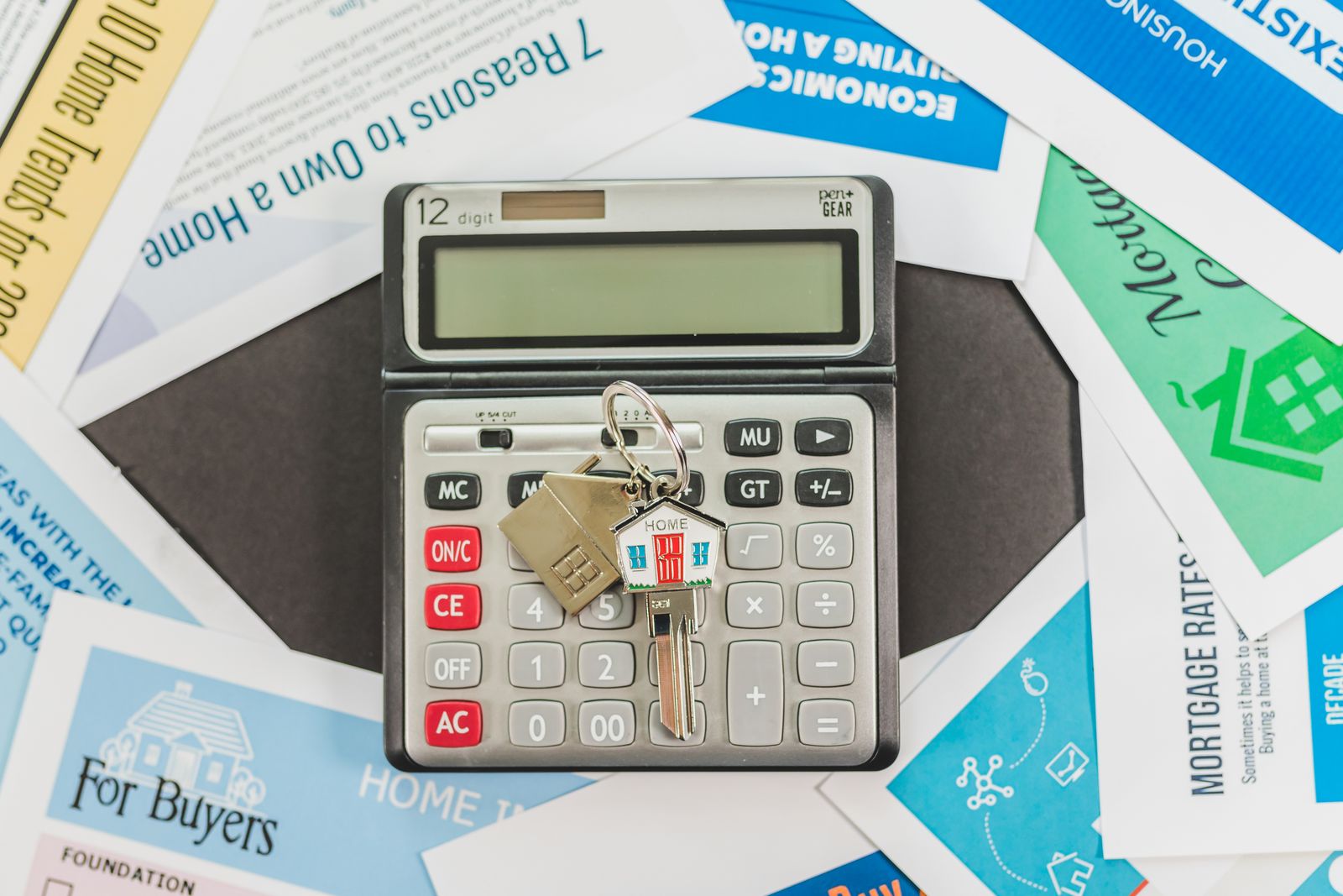 Hausschlüssel liegen auf einem Taschenrechner zwischen Unterlagen zum Immobilienkauf.